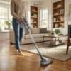 Vacuum cleaner in use in a bright, modern living room with wooden flooring and comfortable furniture.